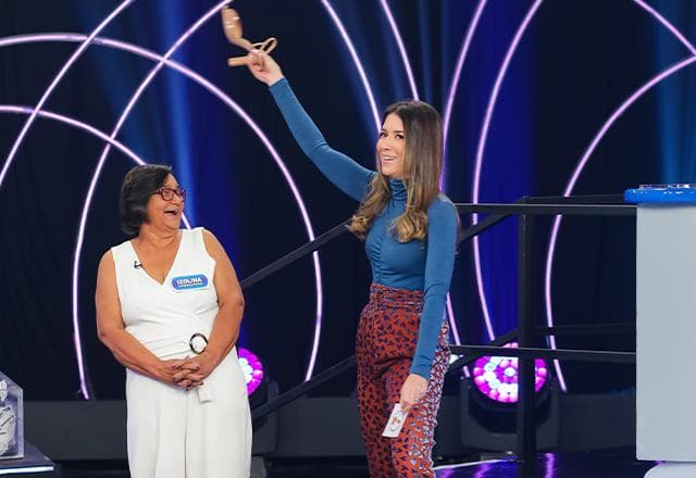 rebeca sorrindo com um sapato na mão ao lado de uma mulher de branco